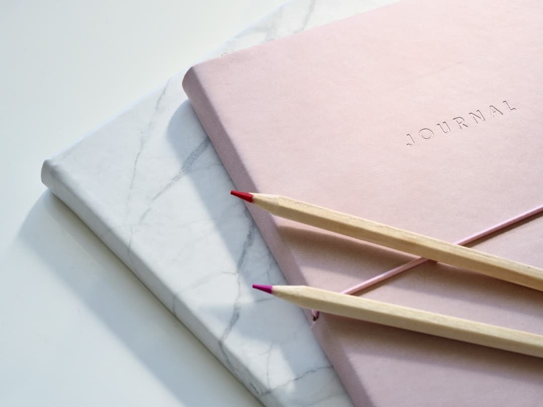 A journal, featuring a blank notebook, and pens, on a desk.